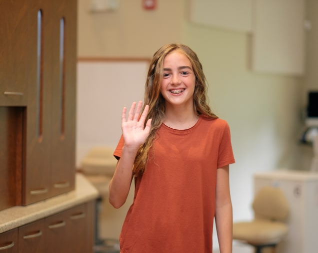 A teenager smiling with her new braces while saying hello