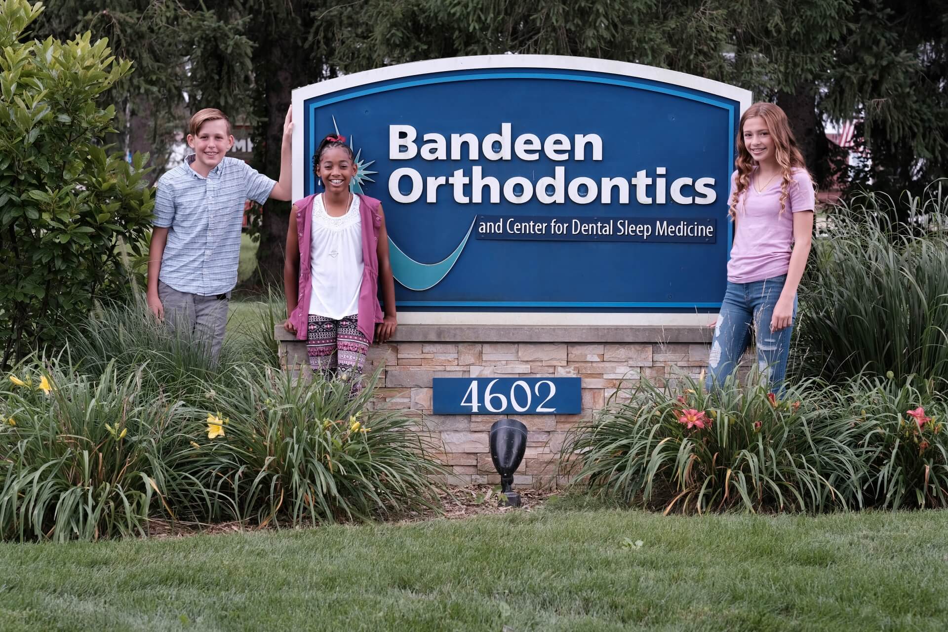 The photo shows 3 young people, two boys and a girl standing near the Bandeen logo